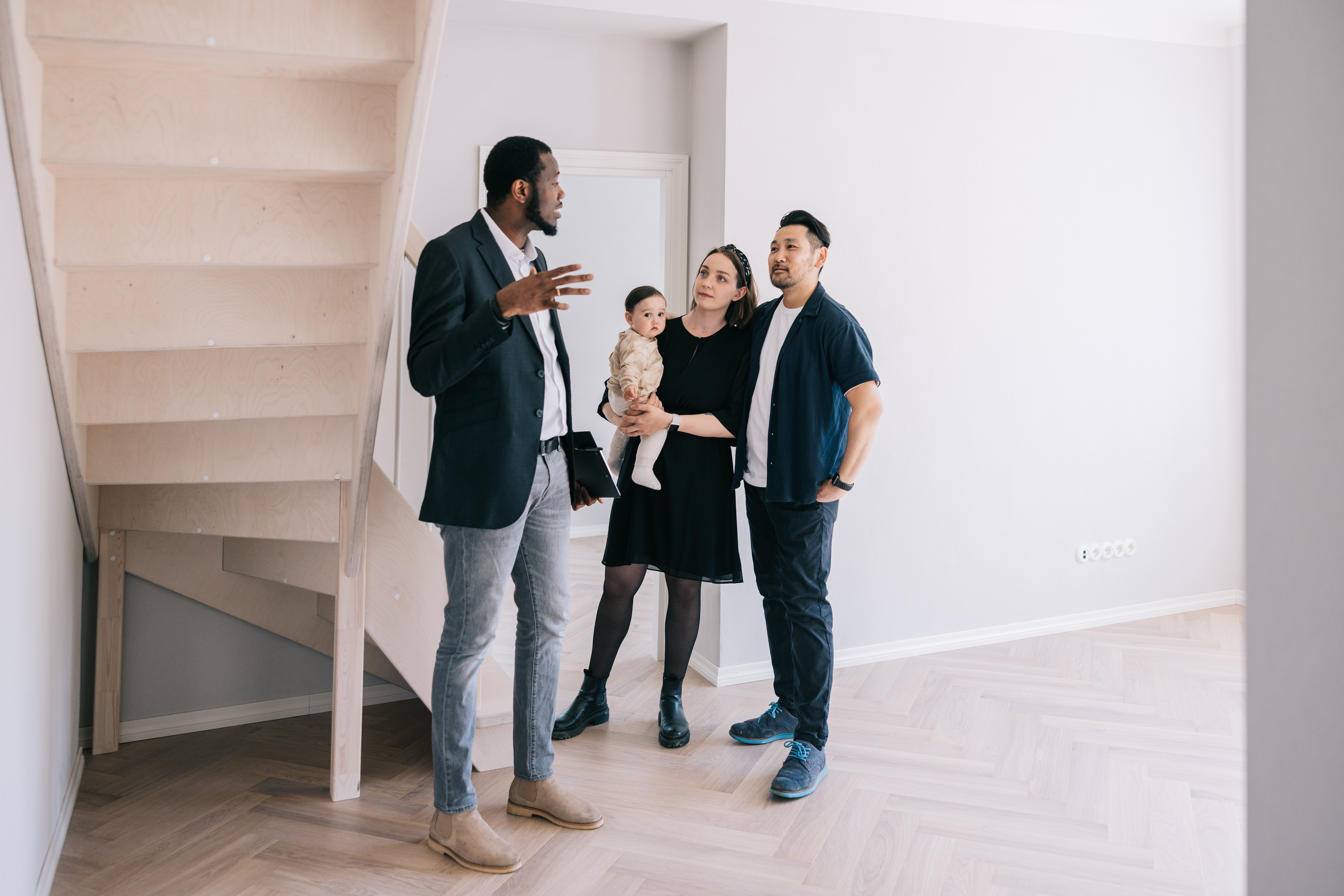 Realtor speaking with couple and baby inside hallway of a home for sale.