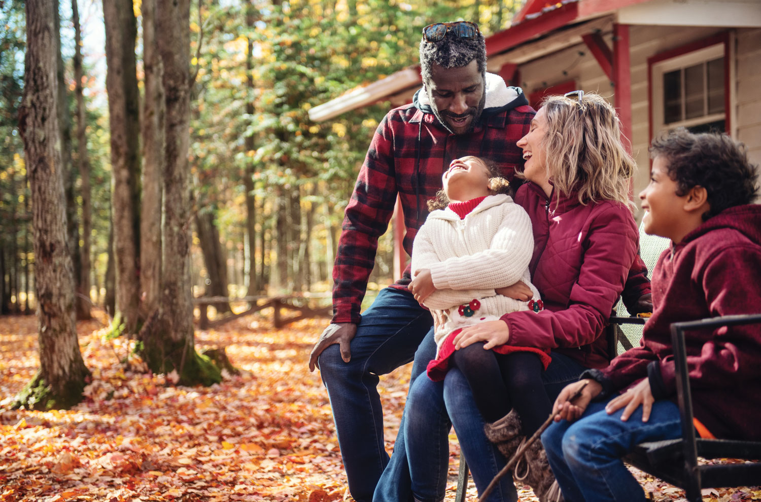 Family laughing together outside of log cabin with fall leaves