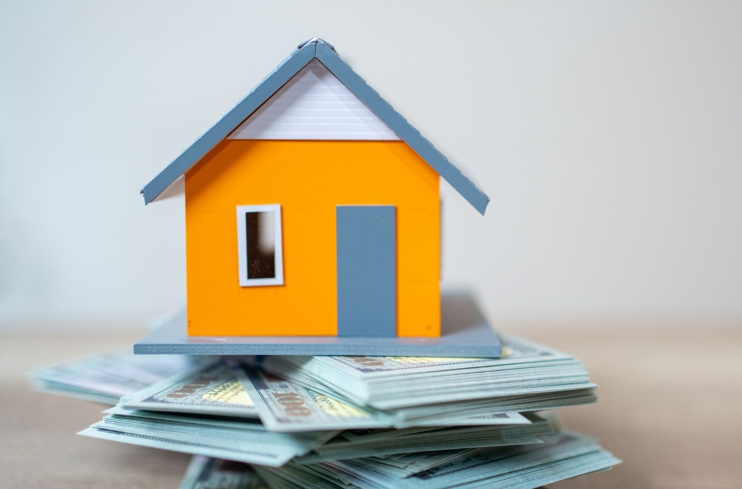 Small model house sitting atop stacks of U.S. dollars