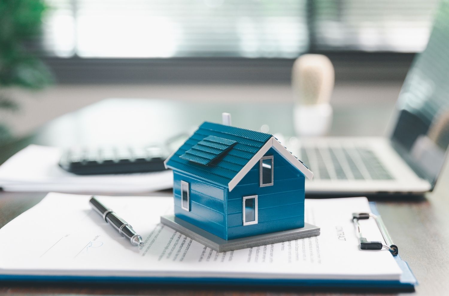 Blue model house sitting on clipboard next to laptop