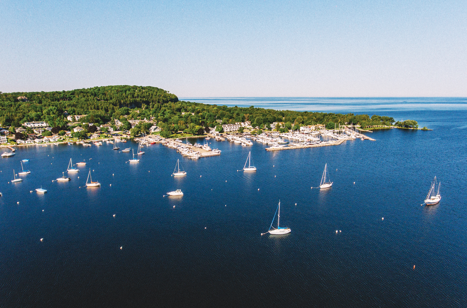 Drone view of scattered sailboats in water near a lake shoreline