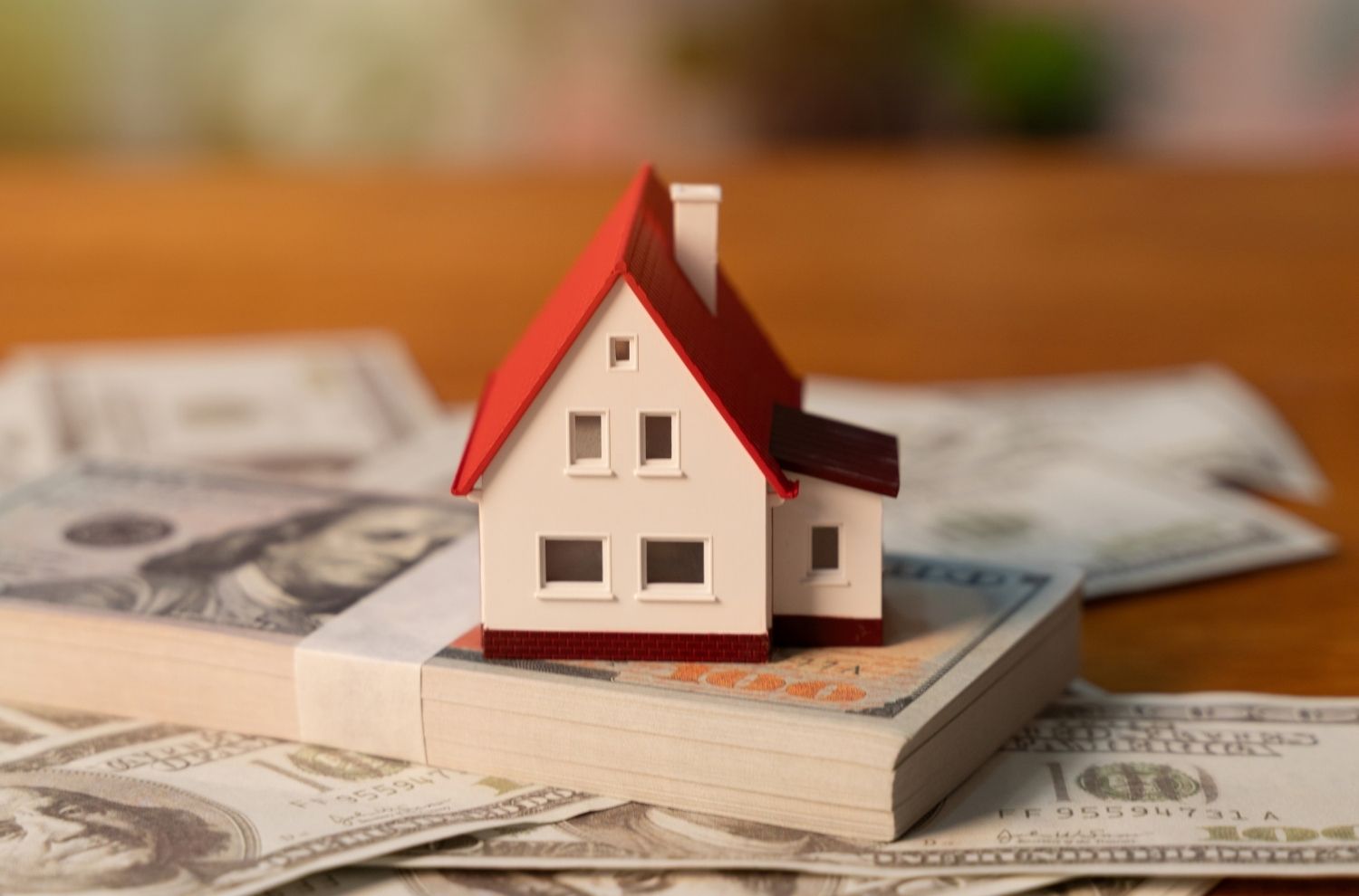 Miniature house sitting atop stack of U.S. dollar bills