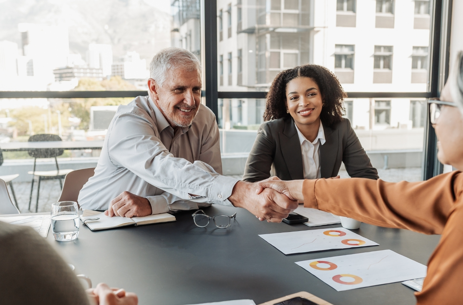 Businesspeople shaking hands at conference table over paperwork