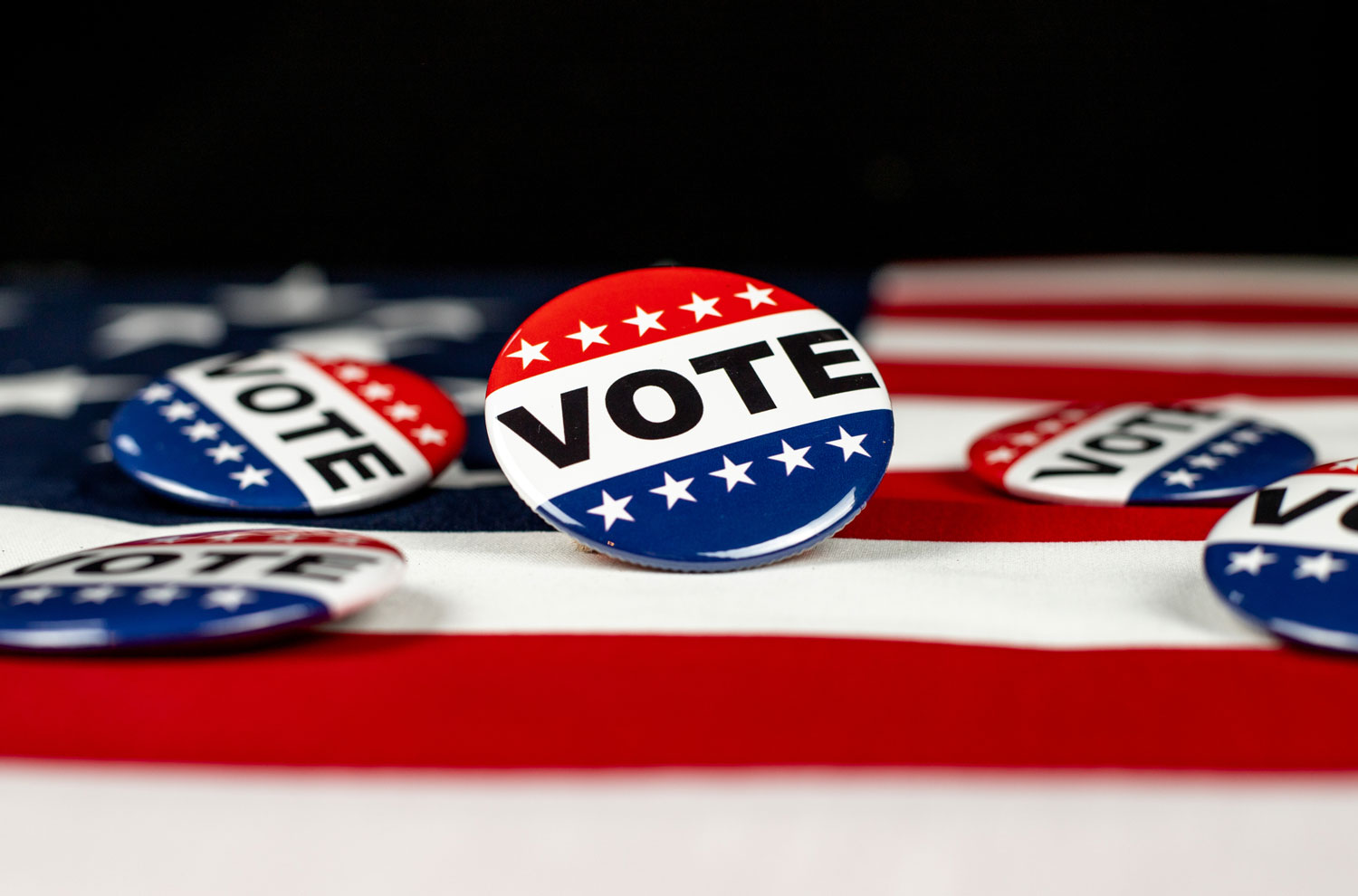Red white and blue vote lapel pins sitting on American flag