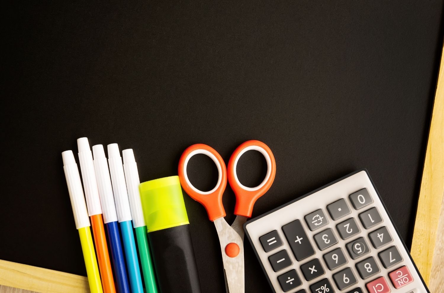 Scissors, markers an other school supplies sitting against small chalkboard